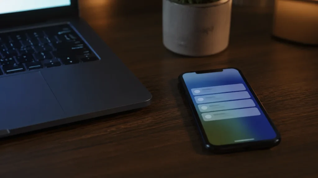 Smartphone affichant une notification d'alerte posé sur un bureau à côté d'un ordinateur